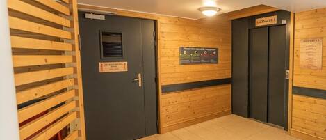 Un pasillo con paneles de madera, dos puertas de ascensor con la etiqueta "ASCENSEUR 1" y un letrero que indica "APARTMENTS 301 + 316".