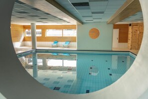 Une piscine intérieure avec un sol carrelé, des murs en bois et deux fauteuils bleus.