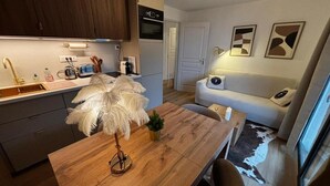 Ett kompakt kök med moderna vitvaror, en matplats med ett träbord och stolar samt ett vardagsrum med en soffa och ett soffbord.