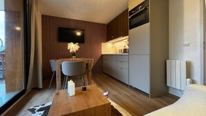 Ett modernt hotellrum med ett matbord i trä, en platt-TV, ett litet kök och ett stort fönster.