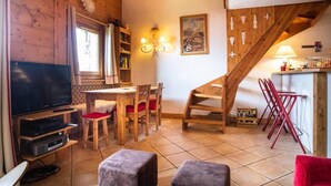 Ein gemütliches Wohnzimmer mit Fernseher, Holzmöbeln, einer Treppe und einem Essbereich.