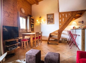 Ein gemütliches Wohnzimmer mit Fernseher, Holzmöbeln, einer Treppe und einem Essbereich.