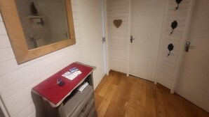Un couloir aux murs blancs, avec un plancher en bois, un miroir doté d’un cadre en bois, un comptoir rouge recouvert de papiers et une porte ornée d’un motif en forme de cœur.