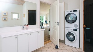 A modern bathroom with a large mirror, white cabinets, a sink, and a stacked washer and dryer. - 4 Star Holiday Home in Tarm (Tarm)