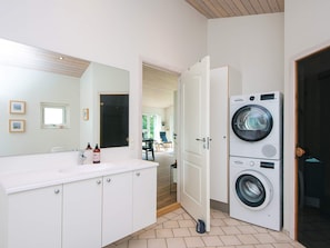 Un bagno moderno con uno specchio grande, mobili bianchi, un lavandino e una lavatrice e asciugatrice affiancate.