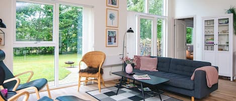 A spacious living room with a large window, a sofa, two chairs, a coffee table, and a bookshelf.