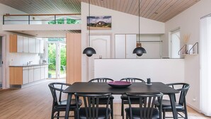 A modern dining area with a large table and chairs, a kitchen in the background, and a view of the outdoors. - 4 Star Holiday Home in Tarm (Tarm)