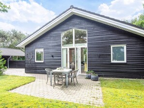 A dark wooden house with a covered patio, a table, and chairs. - 4 Star Holiday Home in Tarm (Tarm)