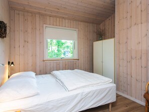 Une pièce aux murs en bois, un lit avec une literie blanche, une fenêtre donnant sur un paysage verdoyant et une armoire.
