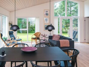 Un vaste espace de vie comprenant une table à manger, des chaises, un canapé et de grandes fenêtres donnant sur l’extérieur.
