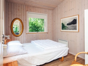 A bedroom with a bed, a window with a view of greenery, a framed picture on the wall, and a wooden floor.
