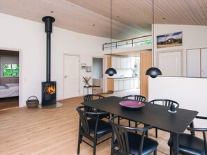 Un intérieur moderne avec une table à manger centrale, des chaises noires, une cheminée bien visible et une cuisine en arrière-plan.