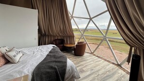 A bedroom with a large window, a bed, a chair, and a small table. - WYnDome - Glamping Dome in Beulah, WY (Beulah)