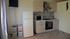 A small kitchen with a microwave, stove, and refrigerator. There are cabinets and a tiled backsplash.