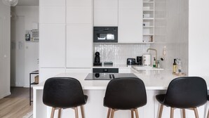 A modern kitchen with white cabinetry, a central island with bar stools, a built-in oven, and a coffee machine. - Modern Top-Floor Apt. in Helsinki (Helsinki)