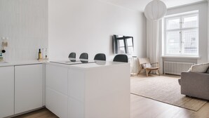 A modern kitchen with white cabinetry, a central island with chairs, a dining area with a sofa, and a large window providing natural light. - Modern Top-Floor Apt. in Helsinki (Helsinki)