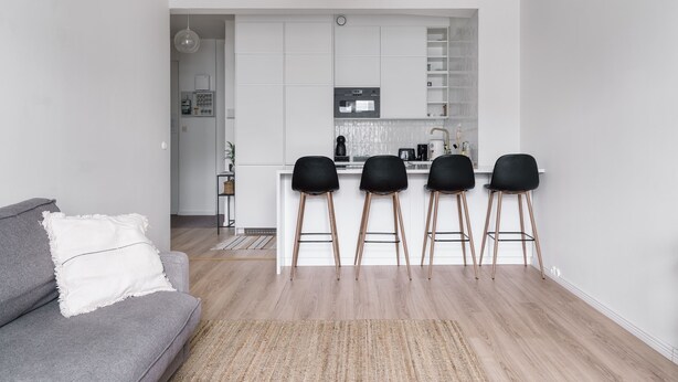 A modern kitchen with white cabinets, a central island with bar stools, and a grey sofa with a white cushion. - Modern Top-Floor Apt. in Helsinki (Helsinki)