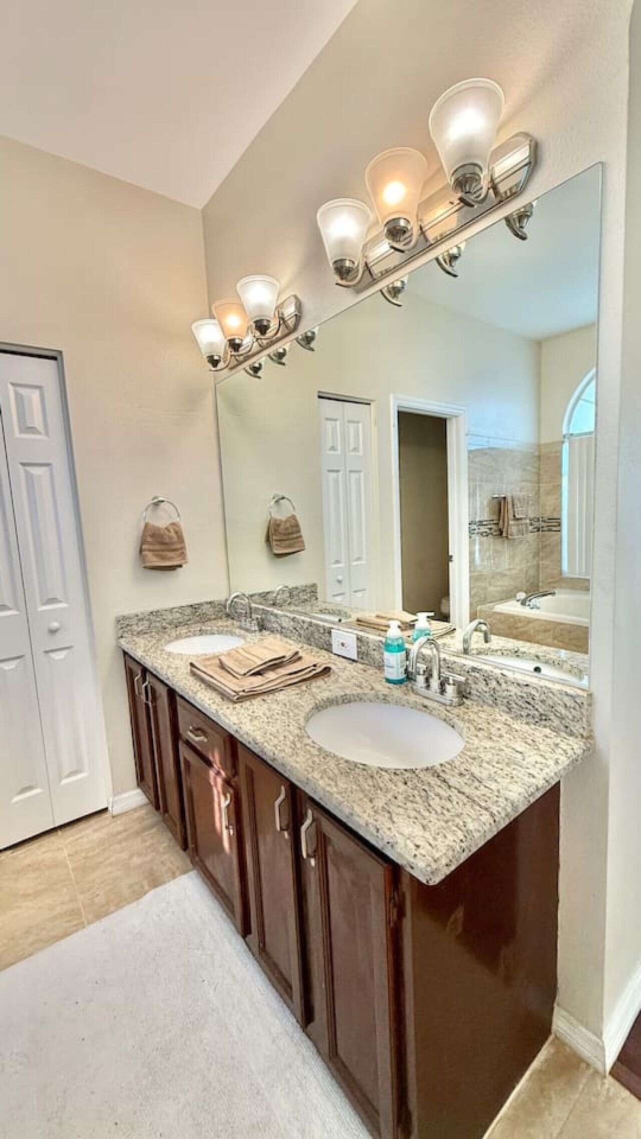A bathroom with a double sink vanity, a large mirror with three lights, and a towel rack.