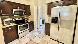 A kitchen with dark wooden cabinets, stainless steel appliances, and a tiled floor. - Spacious House w/ Heated Pool & Hot Tub near Tampa (Brandon)