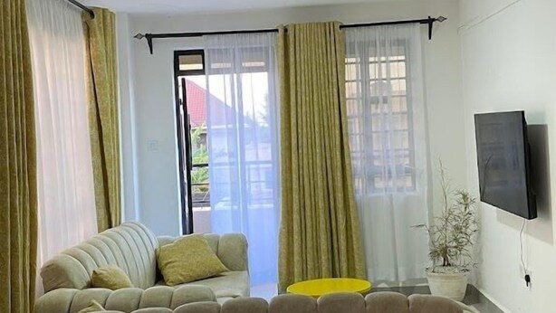 A living room with a beige sofa, a yellow side table, and a black coffee table. - Lux Suites The Urbanite Apartments (Kitengela)