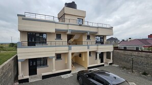 A two-story building with a flat roof, a balcony on the upper floor, and a car parked in front. - Lux Suites The Urbanite Apartments (Kitengela)