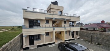 A two-story building with a flat roof, a balcony on the upper floor, and a car parked in front.