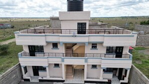 A multi-story building with a central staircase, balconies, and a large water tank on the roof. - Lux Suites The Urbanite Apartments (Kitengela)