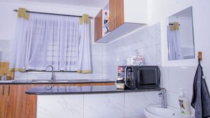 A modern kitchen with a marble countertop, a sink, a microwave, and wooden cabinets. - Lux Suites The Urbanite Apartments (Kitengela)