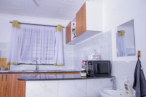 A modern kitchen with a marble countertop, a sink, a microwave, and wooden cabinets.