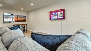 A living room with a gray couch, blue pillows, and a flat-screen TV mounted on the wall displaying a streaming service interface. - Stylish Old Town 2Bd 2Ba Townhome Pool Parking AC Fashion Square (Scottsdale)