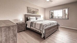 A bedroom with a wooden bed, a nightstand, a ceiling fan, a window with blinds, and a painting on the wall. - Stylish Old Town 2Bd 2Ba Townhome Pool Parking AC Fashion Square (Scottsdale)
