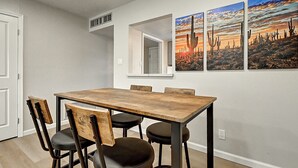 A dining area with a wooden table and chairs, a white door, and a wall with three framed pictures of cacti. - Stylish Old Town 2Bd 2Ba Townhome Pool Parking AC Fashion Square (Scottsdale)