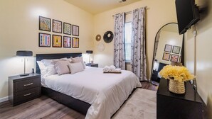 A bedroom with a bed, nightstands, a mirror, and artwork on the walls. - 3BR Getaway Hot Tub, Games & Family Fun (Charlotte)
