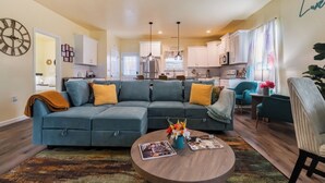 A living room with a sectional sofa, a coffee table with magazines, and a kitchen in the background. - 3BR Getaway Hot Tub, Games & Family Fun (Charlotte)