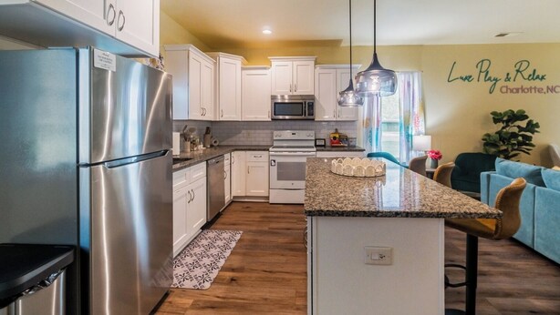 A modern kitchen with stainless steel appliances, white cabinetry, and a granite countertop. - 3BR Getaway Hot Tub, Games & Family Fun (Charlotte)