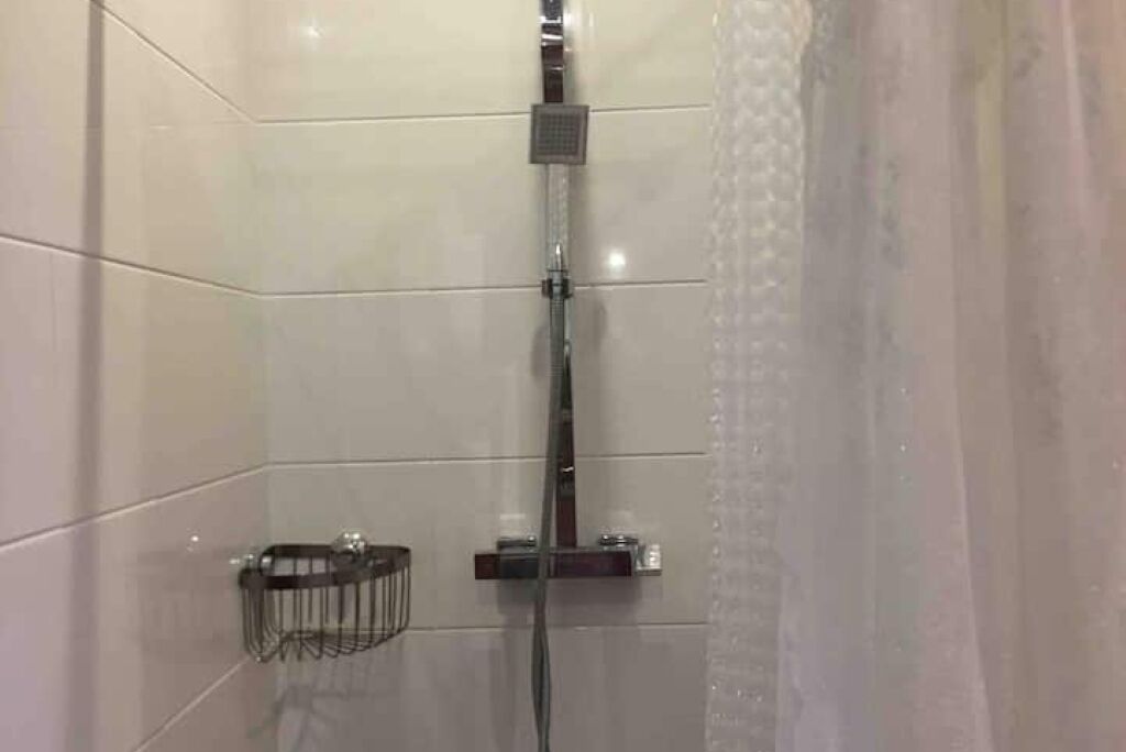 A modern shower with a glass enclosure, a handheld showerhead, and a small shelf with toiletries.