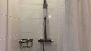 A modern shower with a glass enclosure, a handheld showerhead, and a small shelf with toiletries.