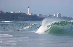 A coastal scene with a large wave, a lighthouse, and buildings in the background. - Charming cottage Sauna Garden Private parking (bidache)