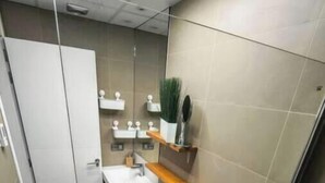 Une salle de bain comprenant des toilettes, un bidet et une baignoire. On y trouve une étagère avec des articles de toilette et un miroir.