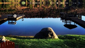 Une scène paisible au bord d’un lac, avec une jetée, un kiosque et un grand rocher au premier plan.