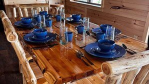 Une table de salle à manger en bois, agrémentée d’assiettes et de verres bleus, entourée de chaises en bois.