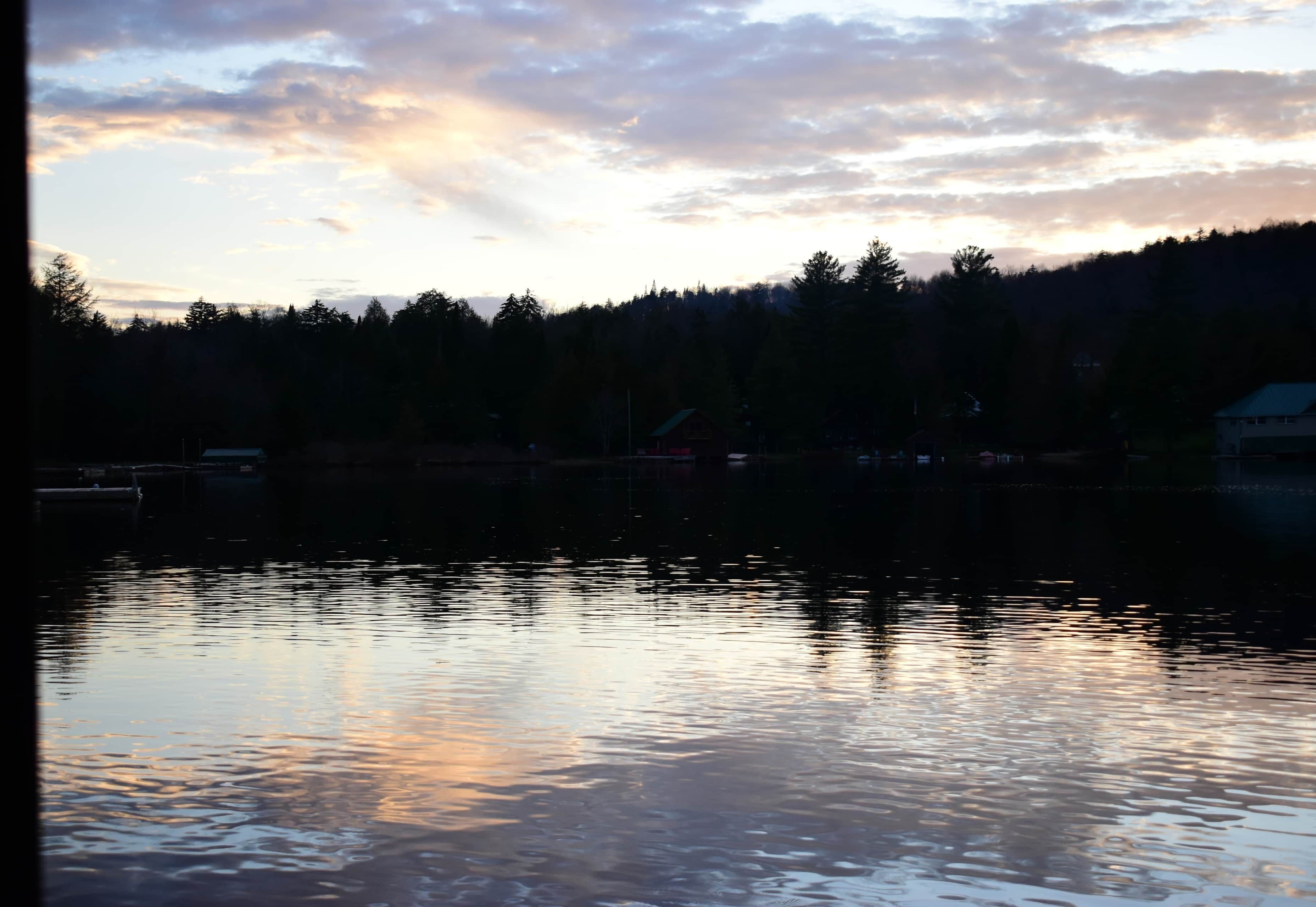A calm lake at sunset with a forested hillside in the background.