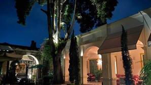 A well-lit outdoor area with a covered seating area, large trees, and a stone pathway.