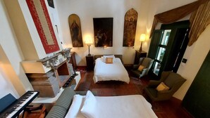 A hotel room with two beds, a piano, a fireplace, and artwork on the walls.