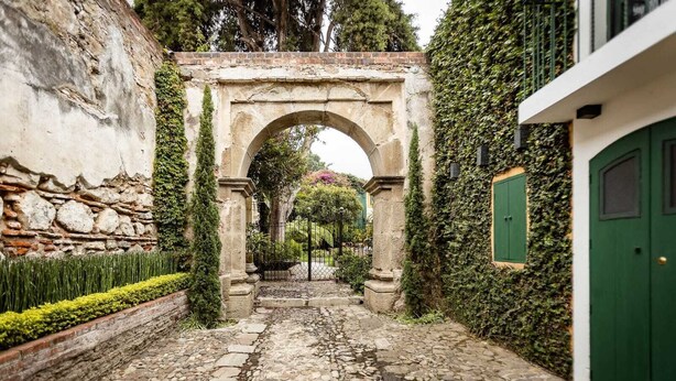 A stone pathway leading through an arched gateway, flanked by a stone wall and a building with a green door.
