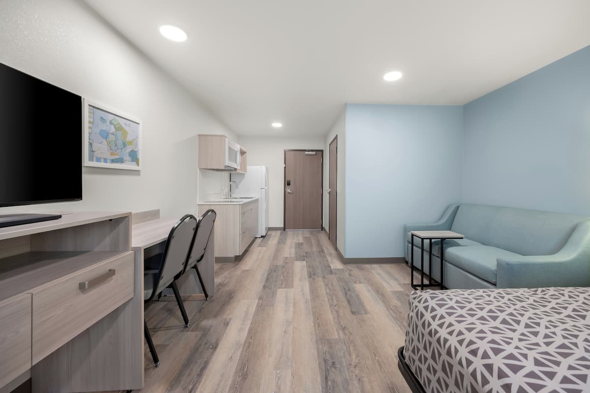 Een moderne hotelkamer met een bed, een bureau, een stoel, een televisie, een magnetron en een klein tafeltje.