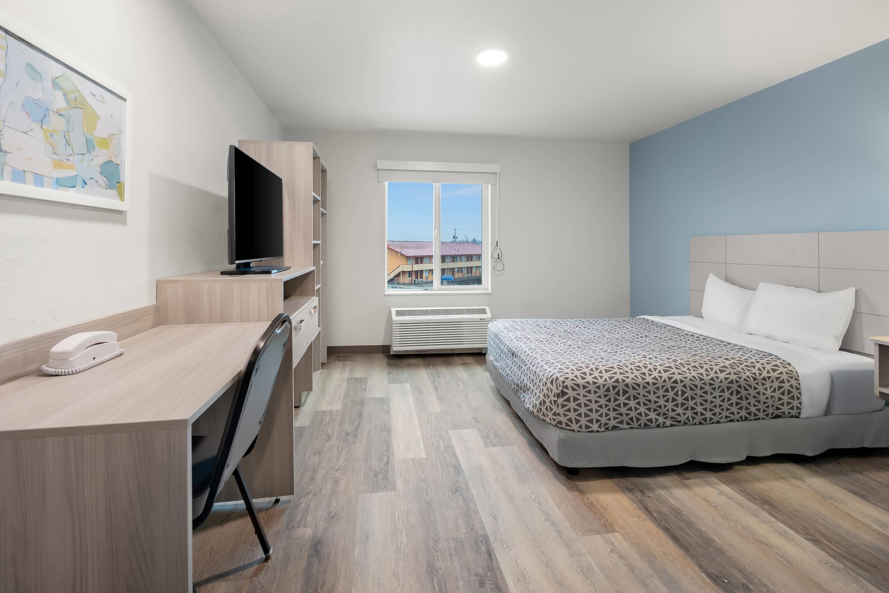 A hotel room with a bed, a desk, a television, and a window with a view of buildings.