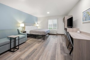 Una habitación de hotel moderna con cama, escritorio, silla, televisor y ventana con persianas.