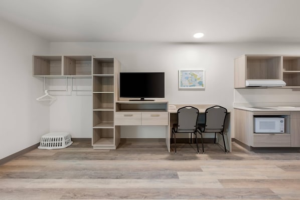 A modern room with a desk, two chairs, a TV, and built-in shelving. - WoodSpring Suites Medford near I-5 (Medford)