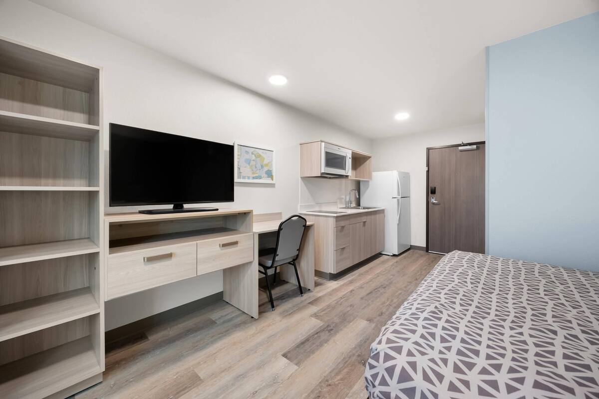 Een compacte kamer met een bed, een bureau met televisie, een kitchenette en een kledingkast.
